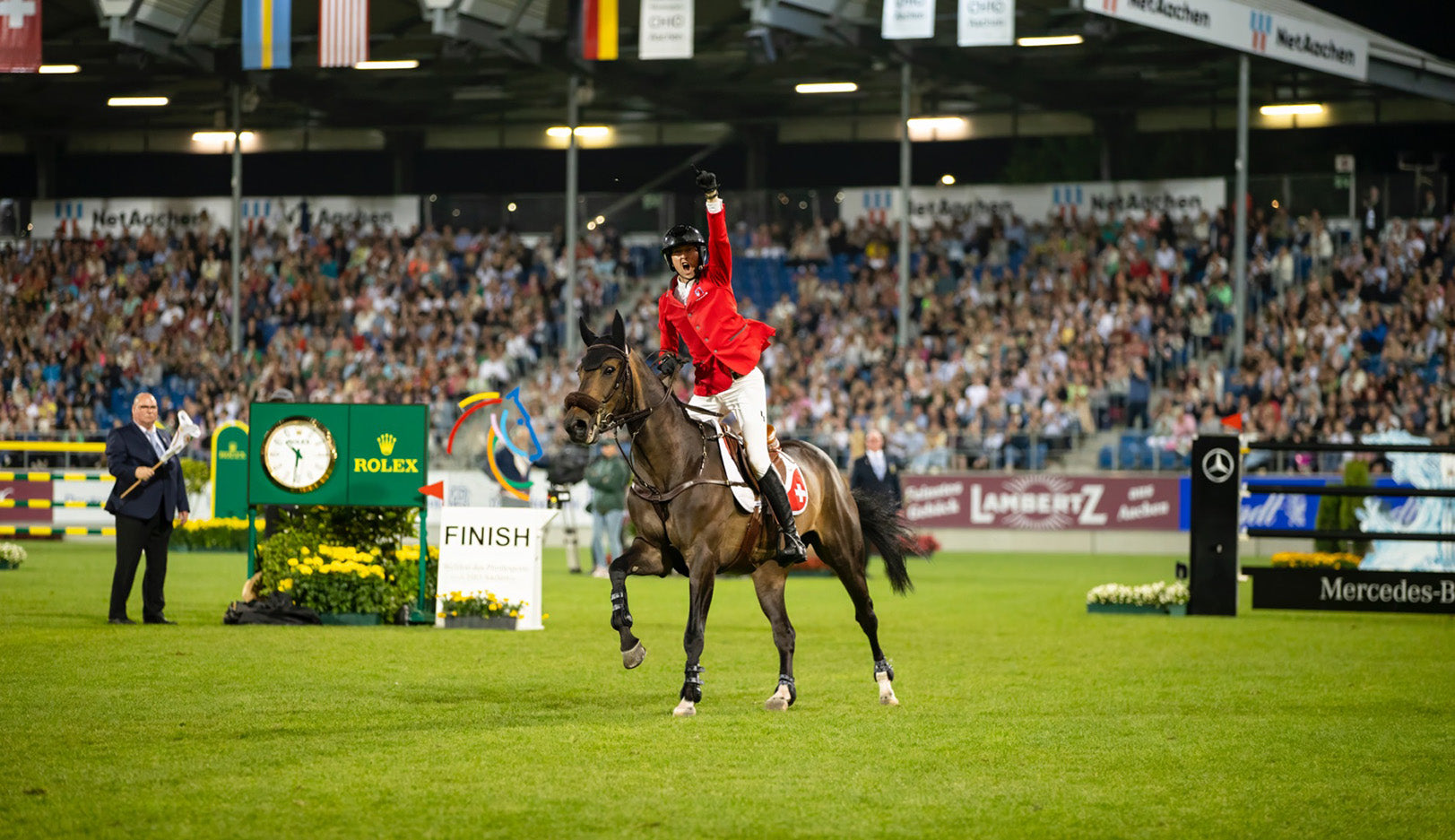 Male equestrian in red jacket celebrating with fist in the air riding on brown horse at end of course