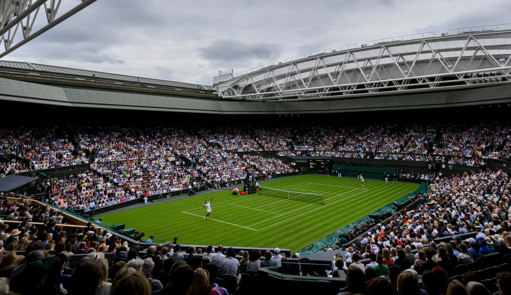 Packed green Wimbledon tennis court stadium, male player making serve