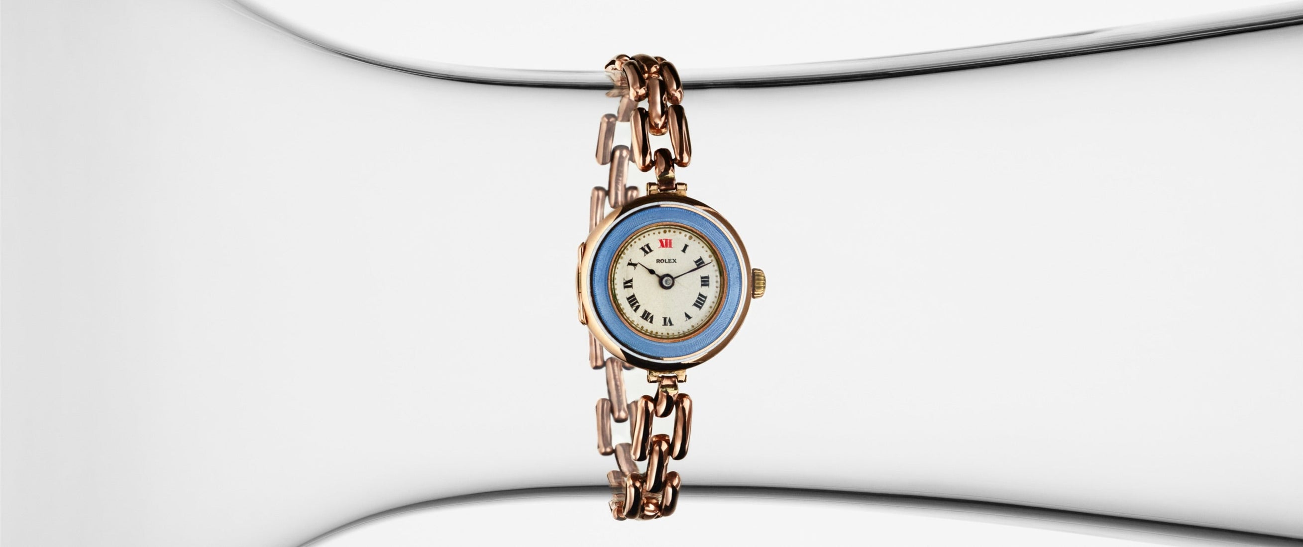 Vintage Rolex women’s wristwatch with blue bezel and Roman numerals on a delicate gold link bracelet, displayed against a minimalistic white background.