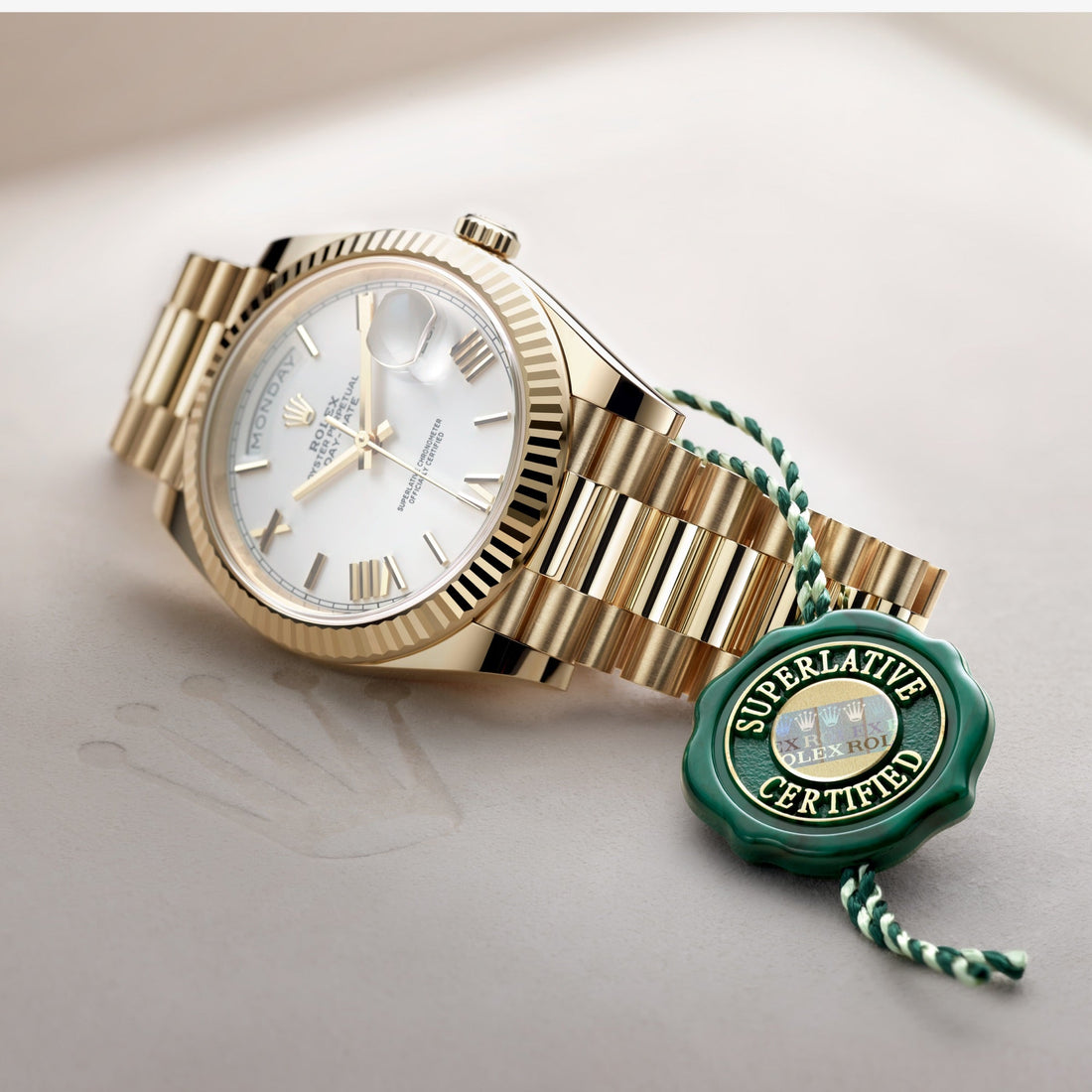 Luxurious yellow gold Rolex Day-Date watch with fluted bezel, white dial, Roman numerals, and a certification seal attached, resting on a light-colored surface.