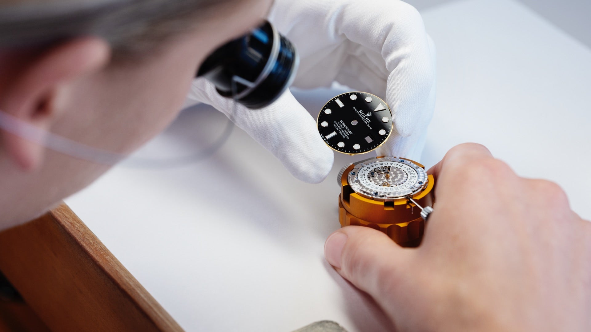 Rolex-trained male watchmaker with magnifier sets black dial face on mechanism