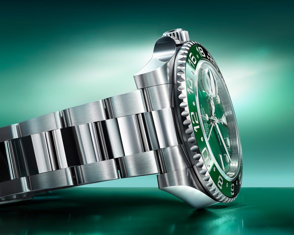 Rolex GMT-Master II watch with green dial and bezel, stainless steel case and bracelet on emerald gradient background