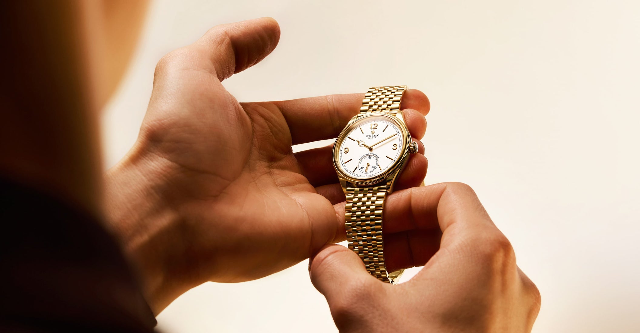 Rolex Perpetual 1908 watch displayed on a textured surface with soft ambient lighting, emphasizing the elegant design and polished finish of the timepiece.