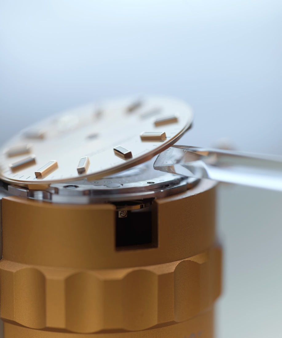 Removal of the dial from the watch movement during the dismantling phase of servicing, ensuring careful handling to maintain the integrity and condition of the dial for accurate reassembly and preservation.