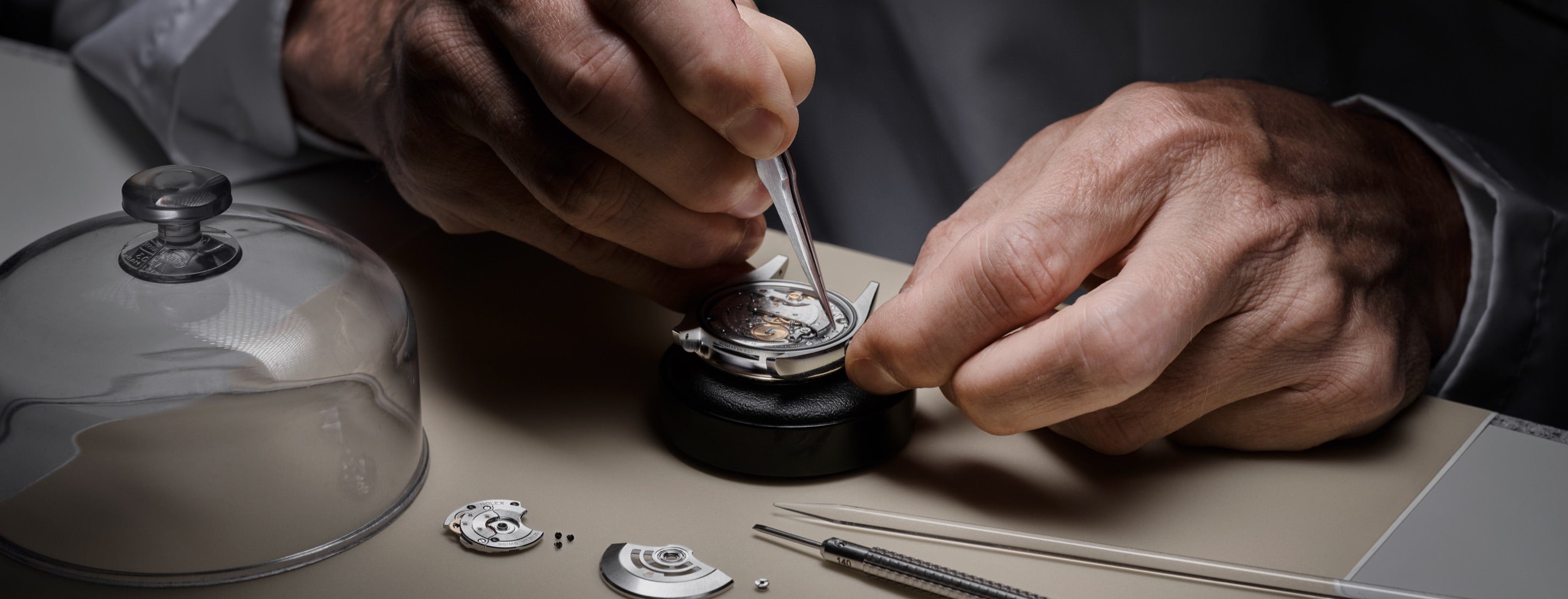 A skilled Rolex technician using precision tools to carefully service and assemble parts of a Rolex watch movement in a well-equipped workshop.