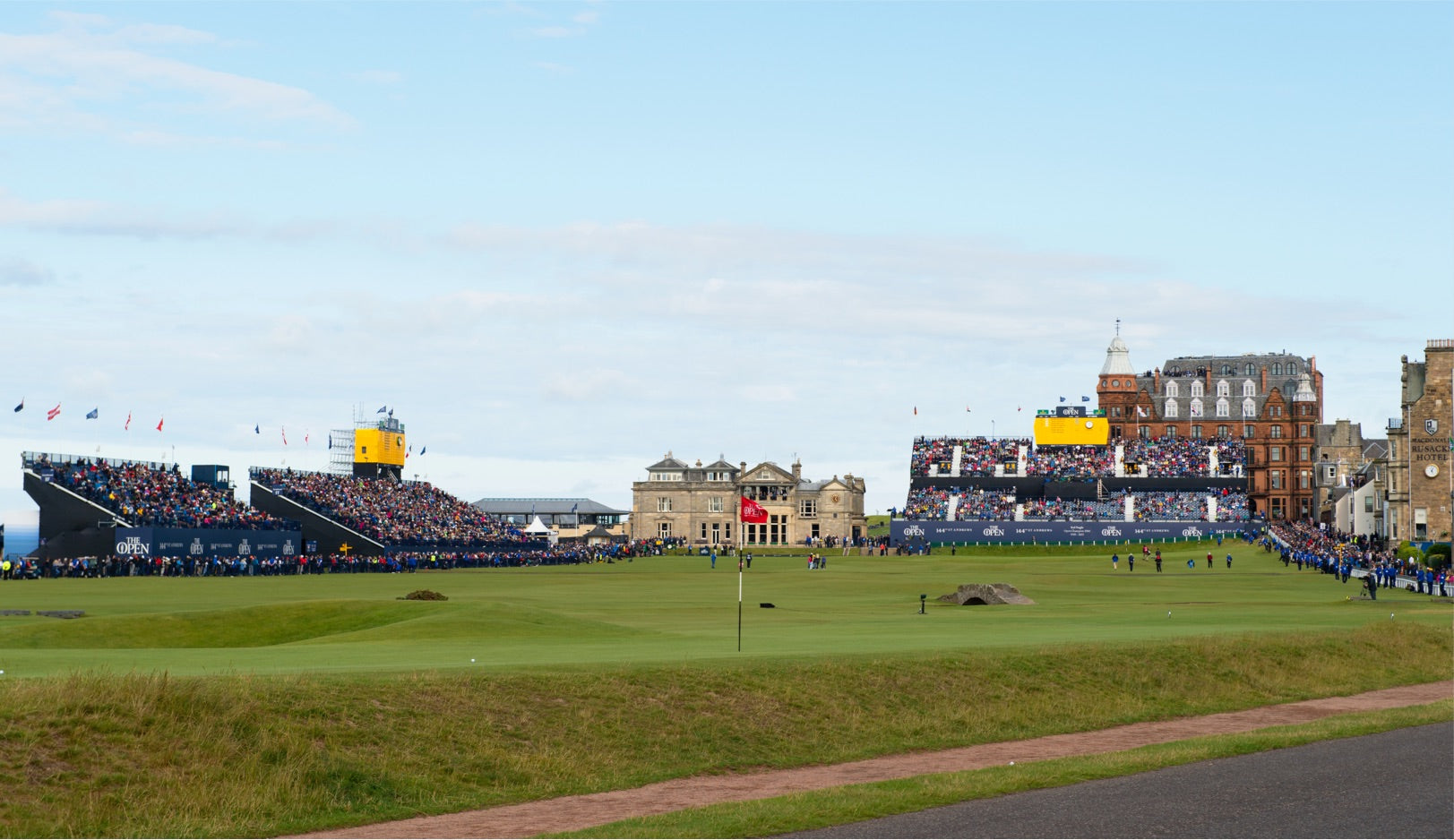 The Open green golf course with red flag in middle of view and packed stands of onlookers